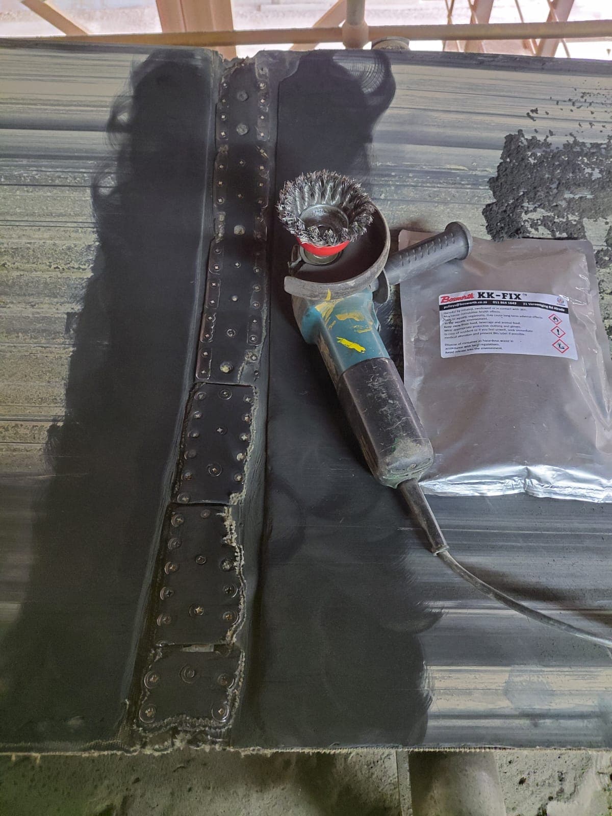 A mechanically fastened conveyor belt splice, wire-brushed and cleaned, with a Bosworth KK-Fix pouch and an angle grinder alongside